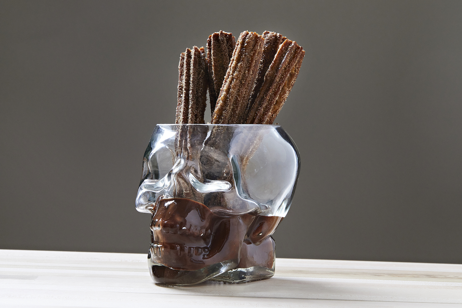 Churros in a skull-shaped glass full of chocolate.