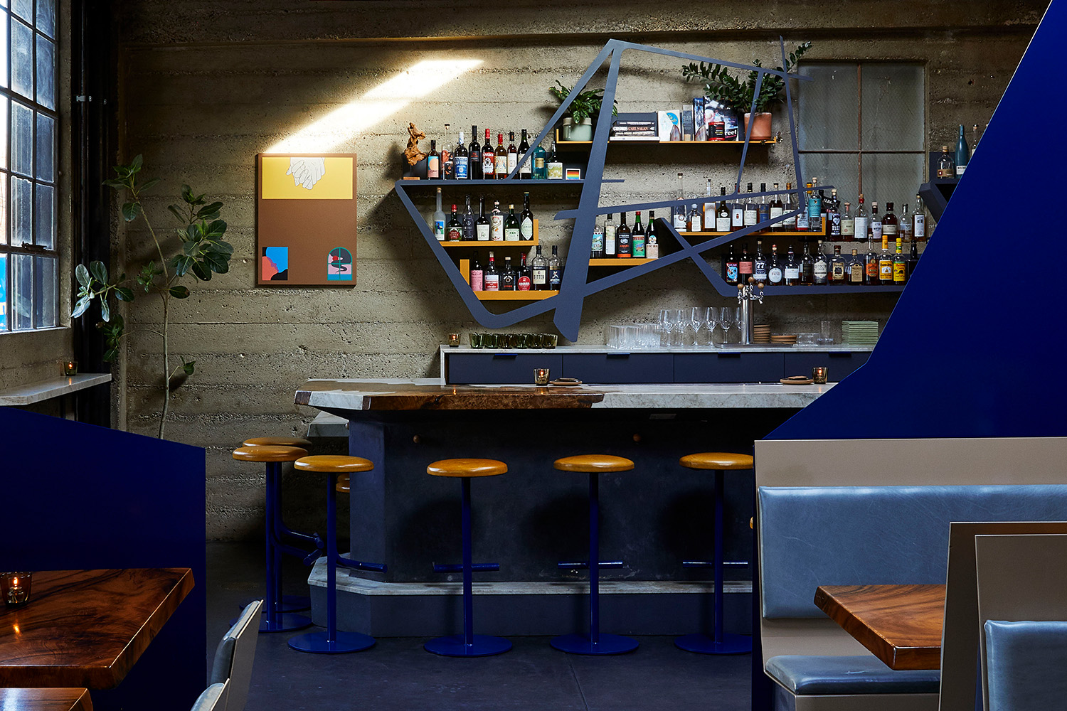 Blue bar against a cement wall with bottles on shelves.