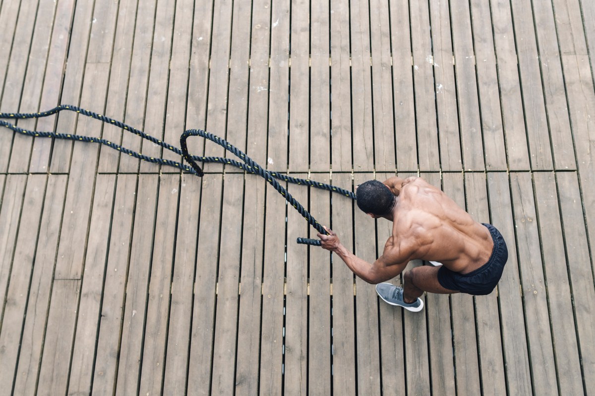 A shirtless man with impressive back muscles using battle ropes.