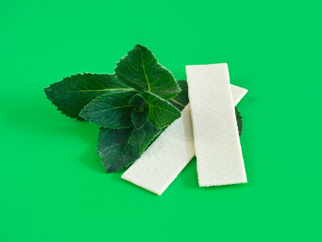 Two sticks of gum next to mint, against a green background.