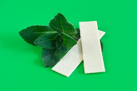 Two sticks of gum next to mint, against a green background.