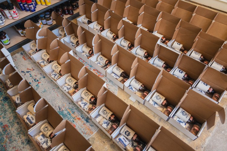 A grid of boxes being filled with sauce and other merchandise for subscription services.