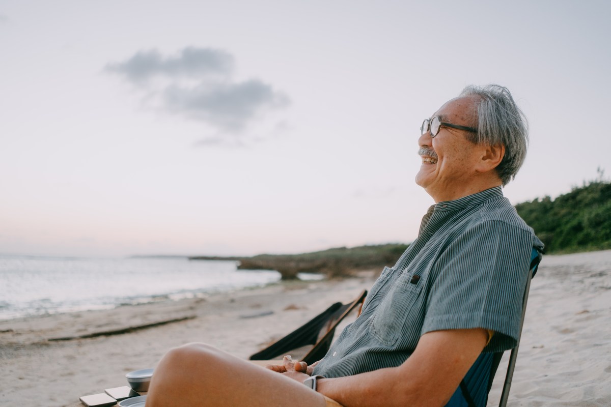 An old man sitting on the beach and smiling.