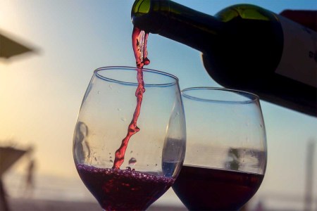 Activities on the sunset. bottle of wine serving wine on two cups on the beach. Red wine is becoming more popular as a summer drink.