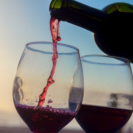 Activities on the sunset. bottle of wine serving wine on two cups on the beach. Red wine is becoming more popular as a summer drink.