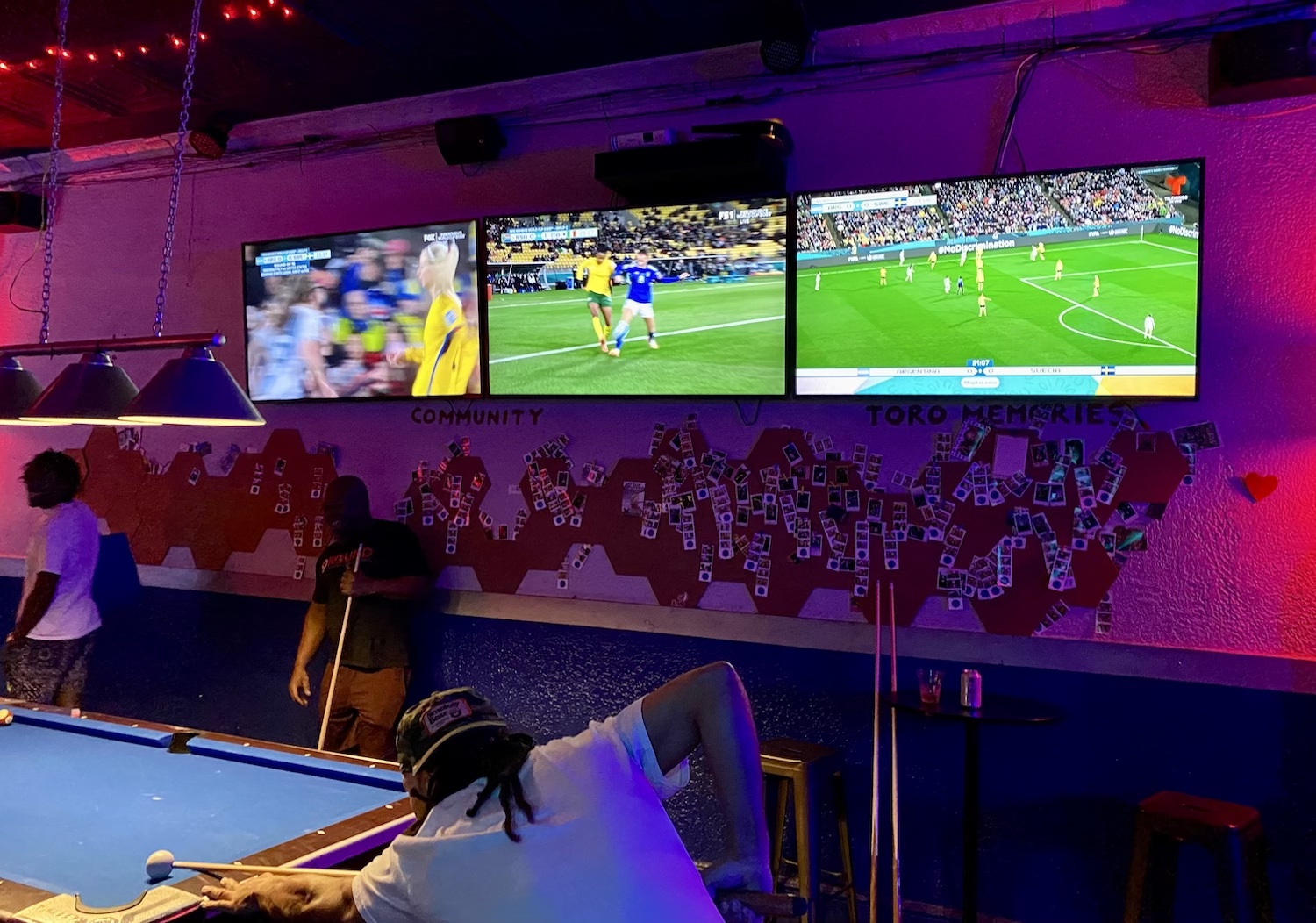 three screens TV in purple-ish lighting at bar
