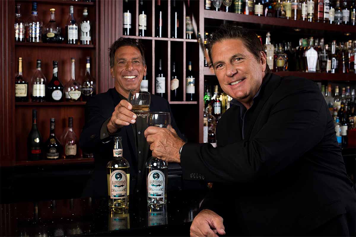 James Robert Morris or Chris Chelios drinking a bottle of their El Bandido Yankee tequila in a bar