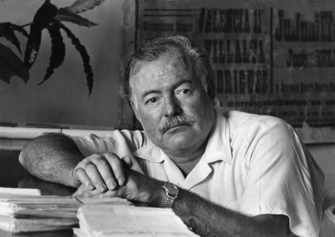 American writer Ernest Hemingway leaning on the desk of his office
