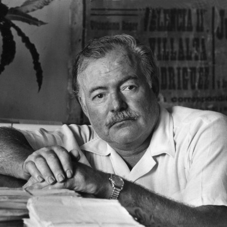 American writer Ernest Hemingway leaning on the desk of his office