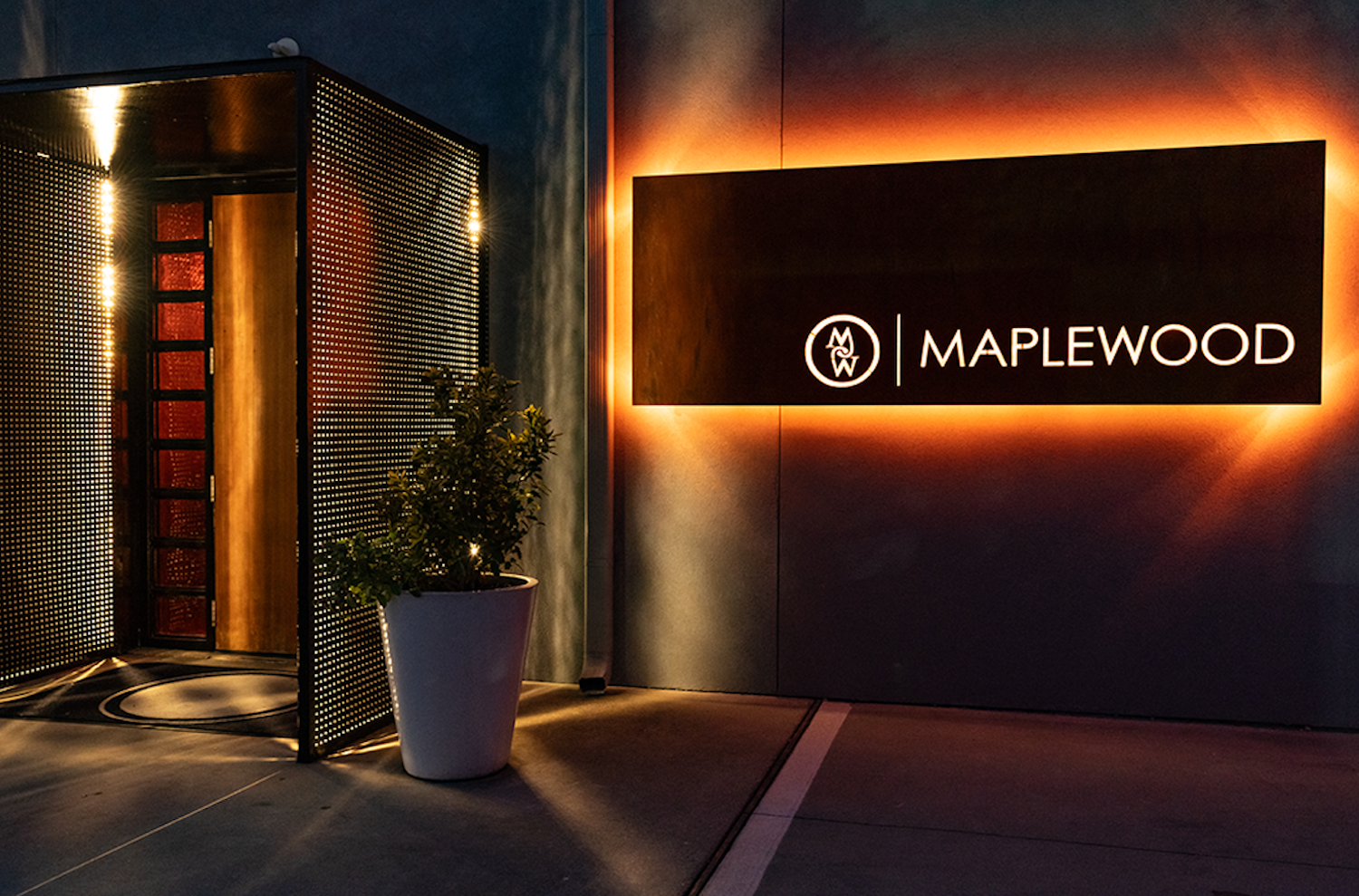 Sign that says "Maplewood" glowing in orange light at a door.