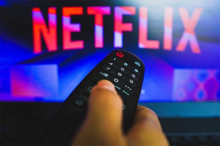 In this photo illustration, a hand holding a TV remote control in front of the Netflix logo on a TV screen.