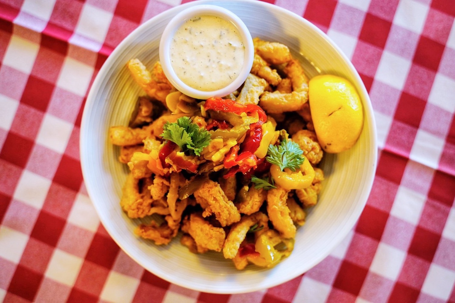 calamari with lemon and peppers in a white bowl on a red and white checkered tablecloth 