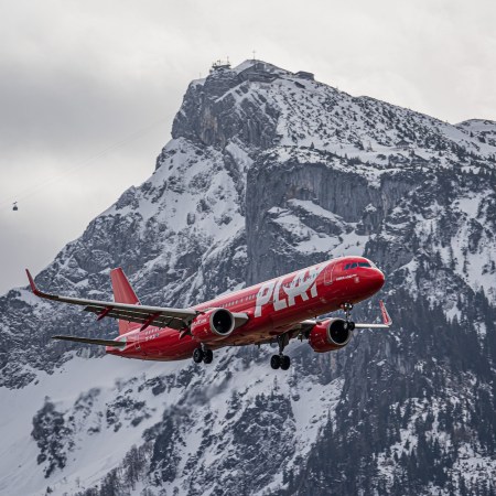A red Play airplane flying in front of snowy mountain
