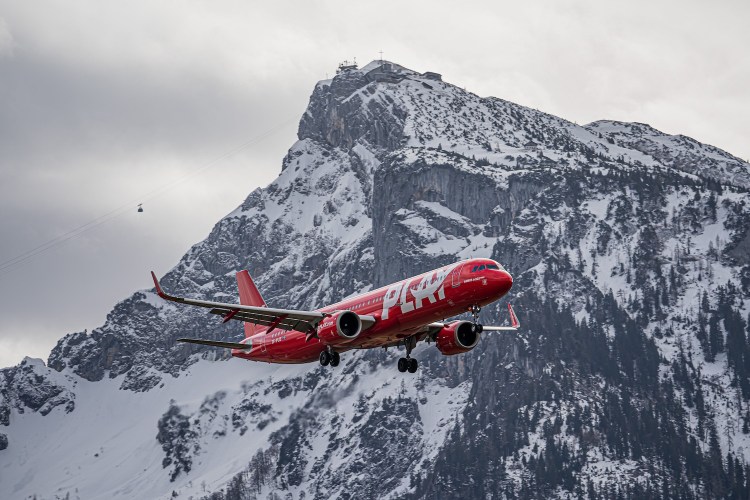 A red Play airplane flying in front of snowy mountain