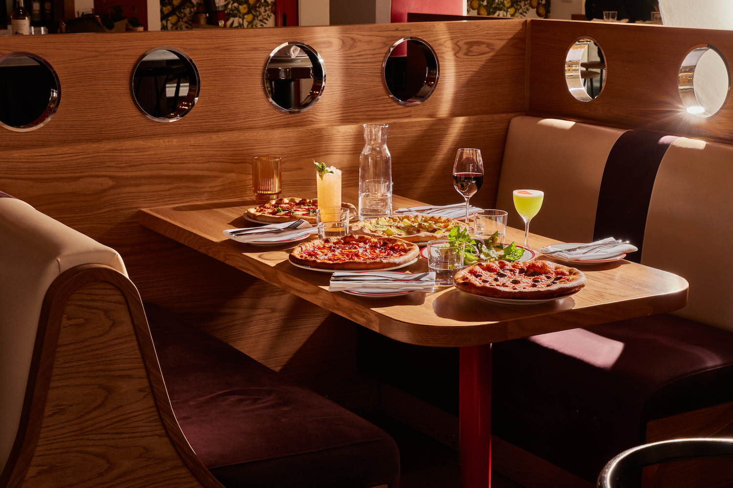 Spread of food and cocktails on a table in a booth seat of Corzetti
