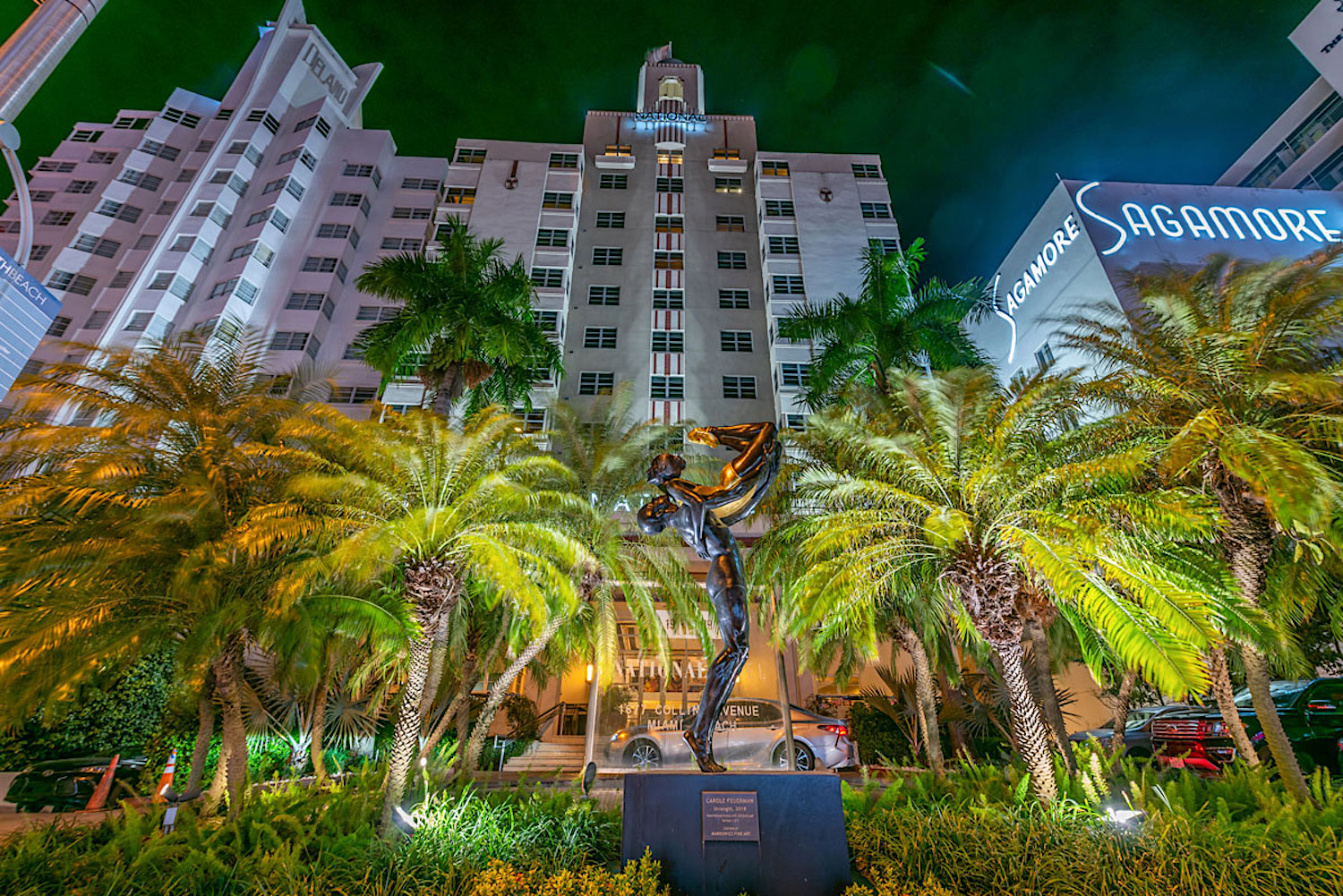 Large hotel building with a statue and palm trees at the front 