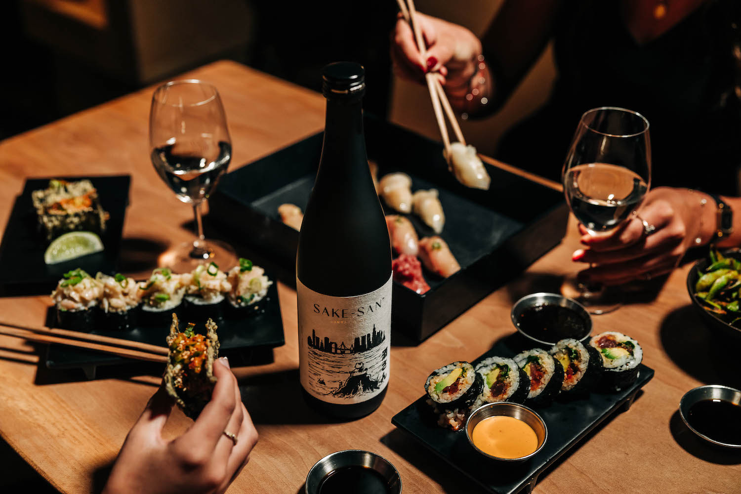 Sushi, wine glasses and a bottle of sake on a table