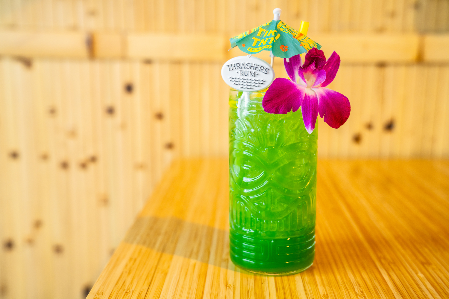 a tropical cocktail in a green tiki glass with a purple orchid and paper umbrella