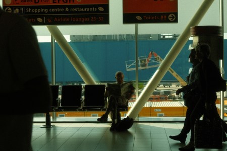 A man sitting cross-legged at the airport gate, reading a newspaper.