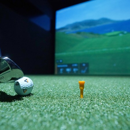A golf club lining up a ball at an indoor golf simulator.