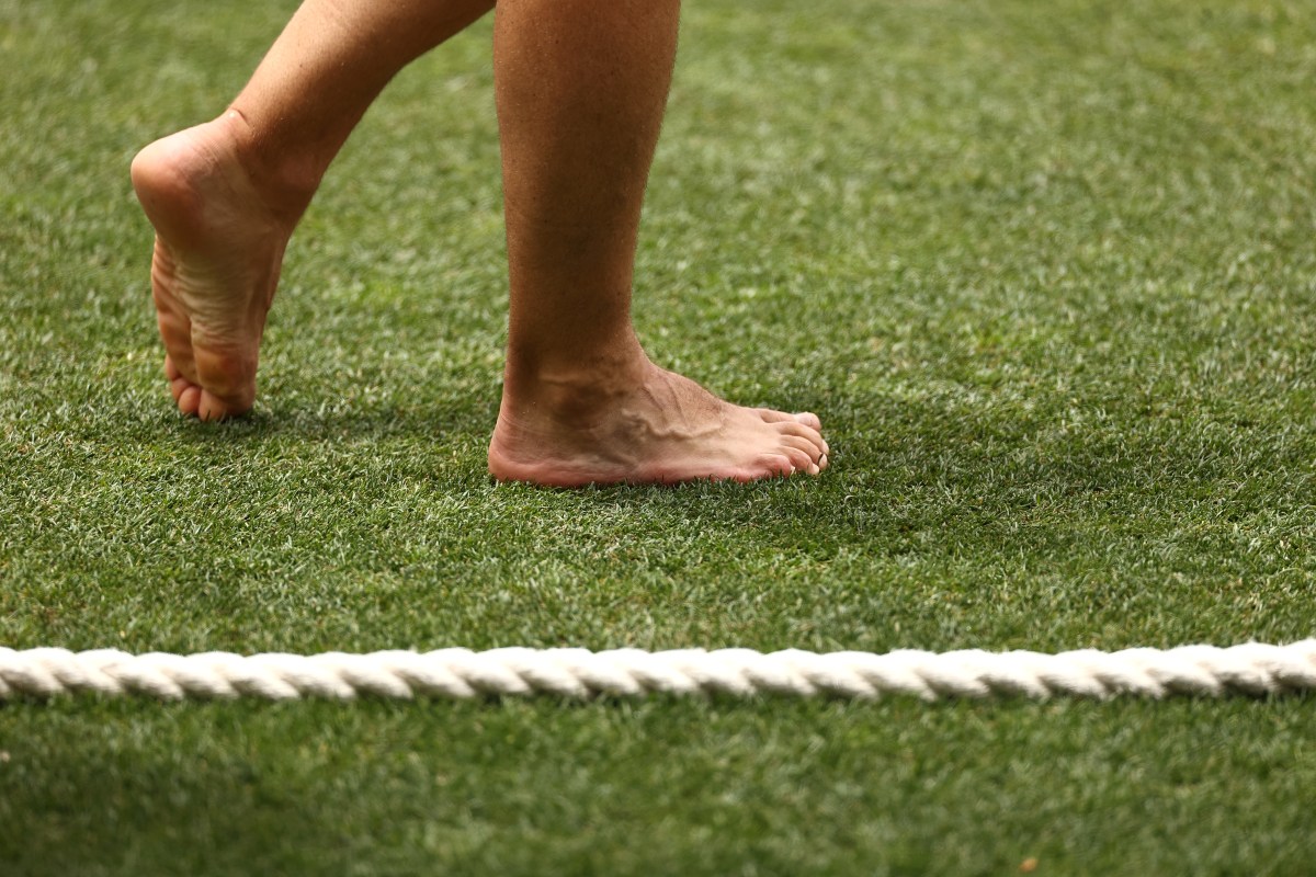 A pair of bare feet walking on a turfed field.