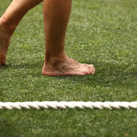 A pair of bare feet walking on a turfed field.