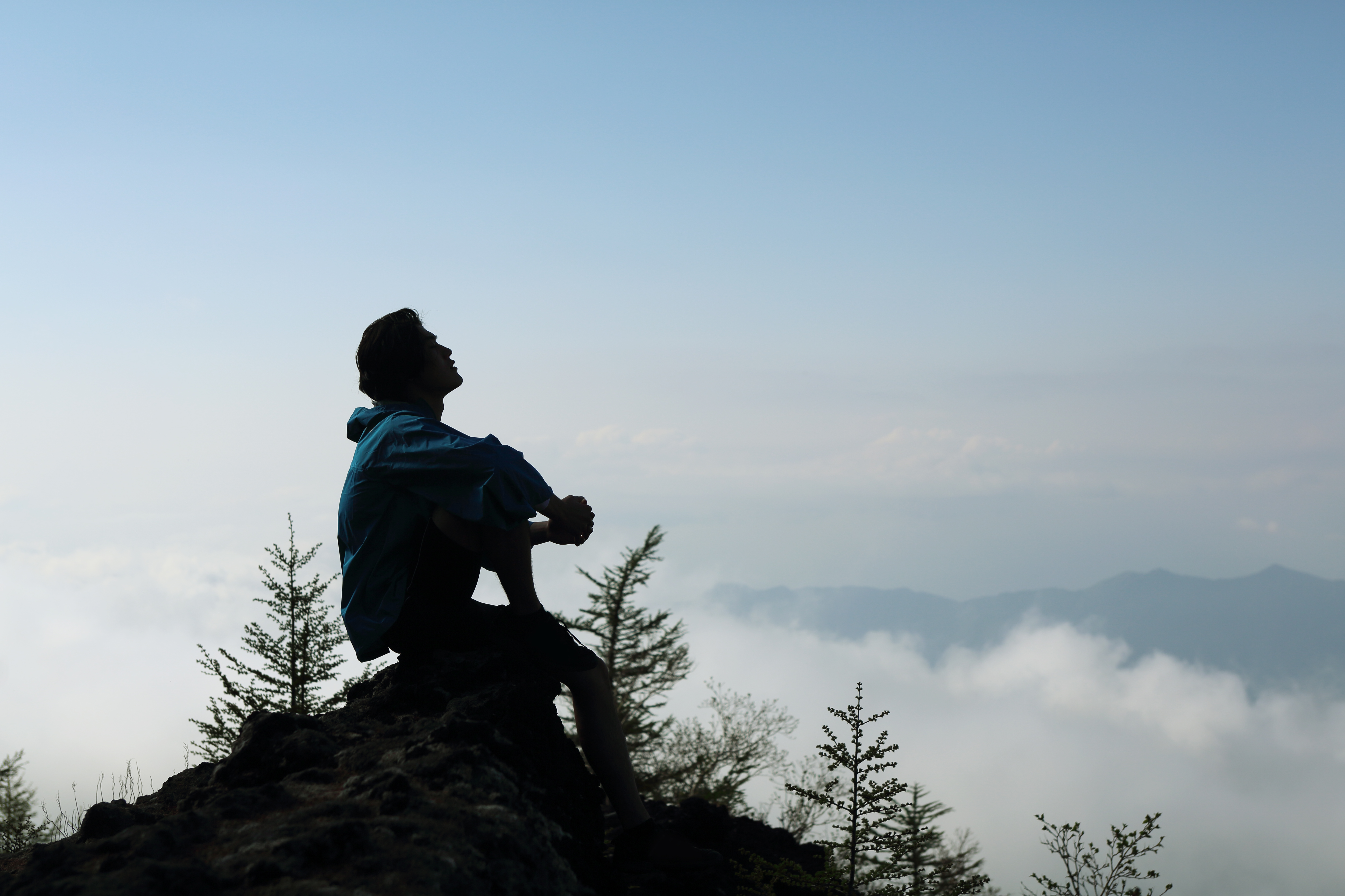 A man sitting on a mountain with the clouds behind him.