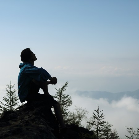 A man sitting on a mountain with the clouds behind him.
