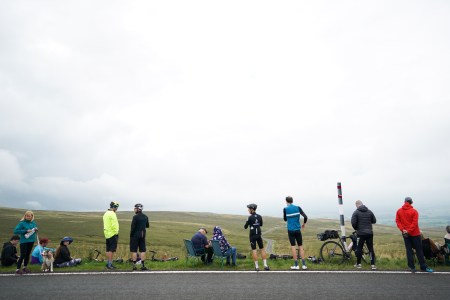 A group of adult men and women standing with bikes and chairs on the side of the road.