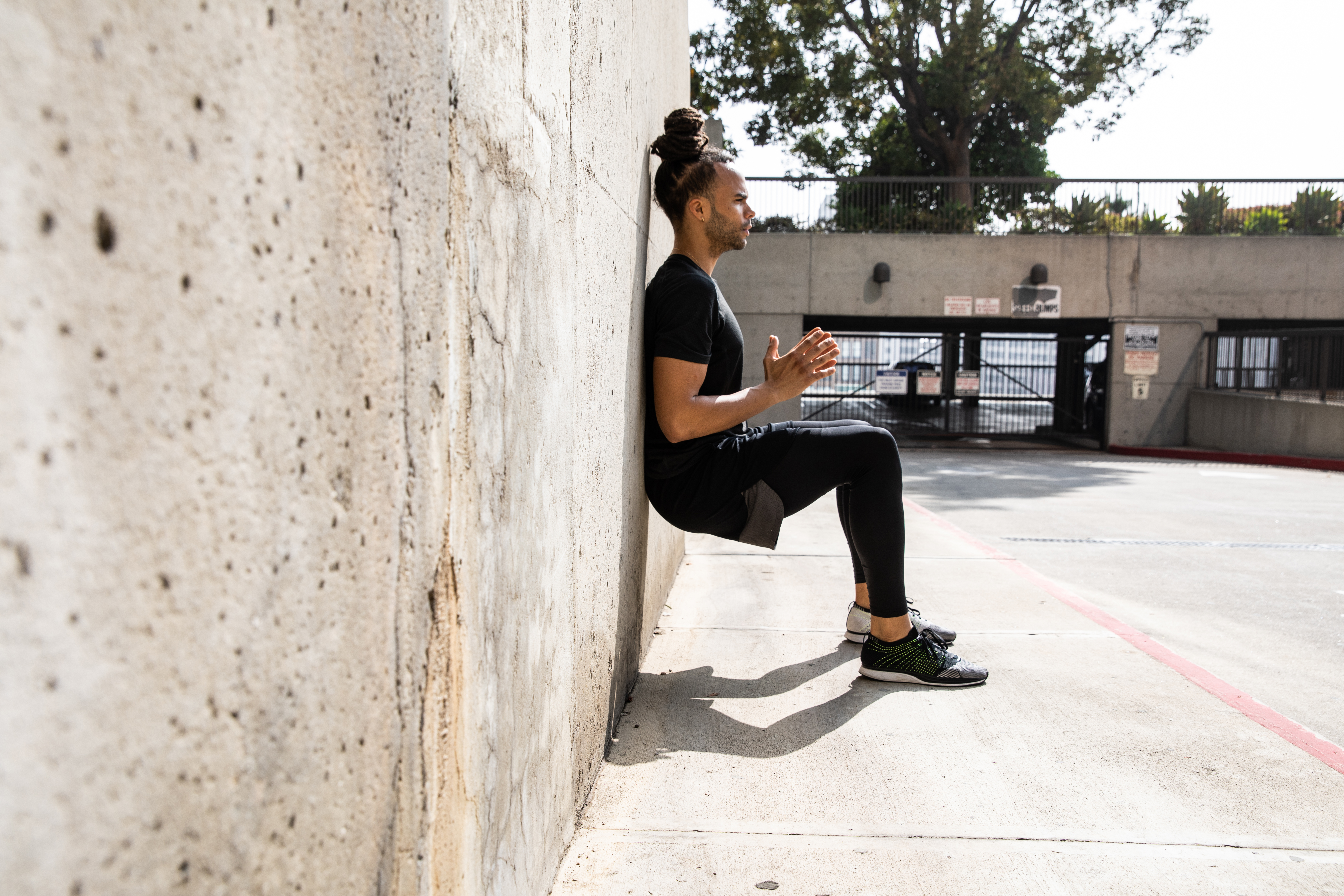 A man performing a wall sit against a concrete wall.