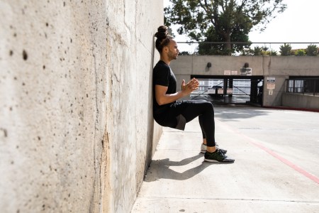 A man performing a wall sit against a concrete wall.
