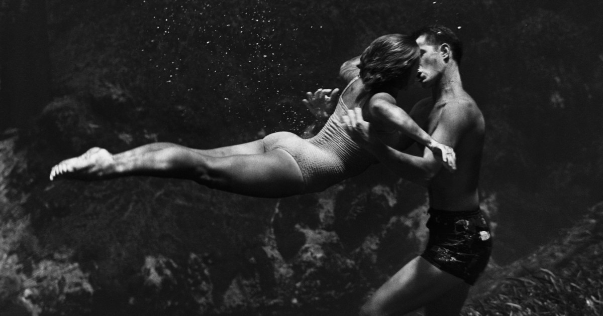 a black and white photo of a man and woman kissing under water