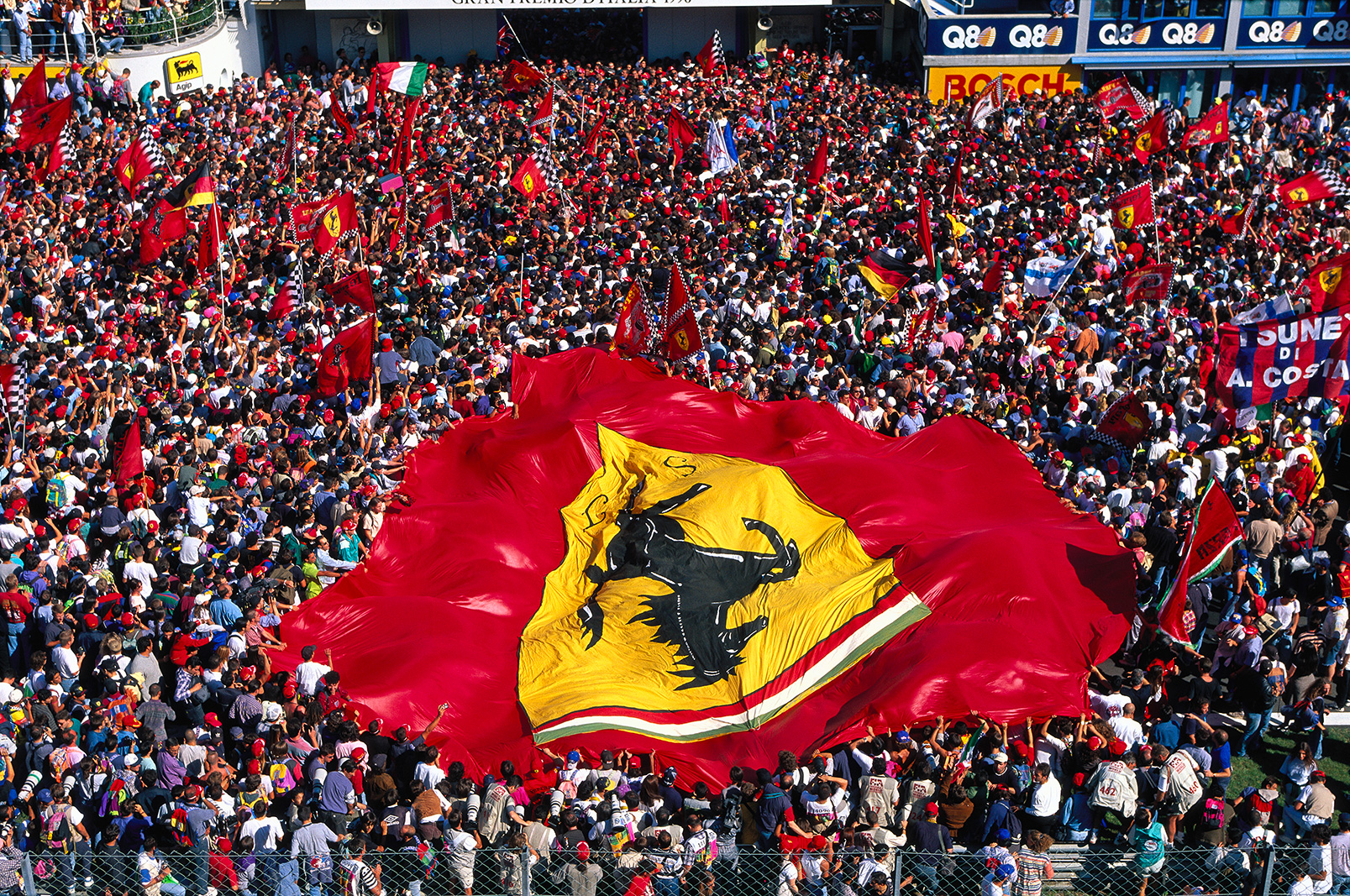 AUTODROMO NAZIONALE MONZA, ITALY - SEPTEMBER 08: The tifosi celebrate in front of the podium with a large Ferrari flag after Michael Schumacher's victory during the Italian GP at Autodromo Nazionale Monza on September 08, 1996 in Autodromo Nazionale Monza, Italy.