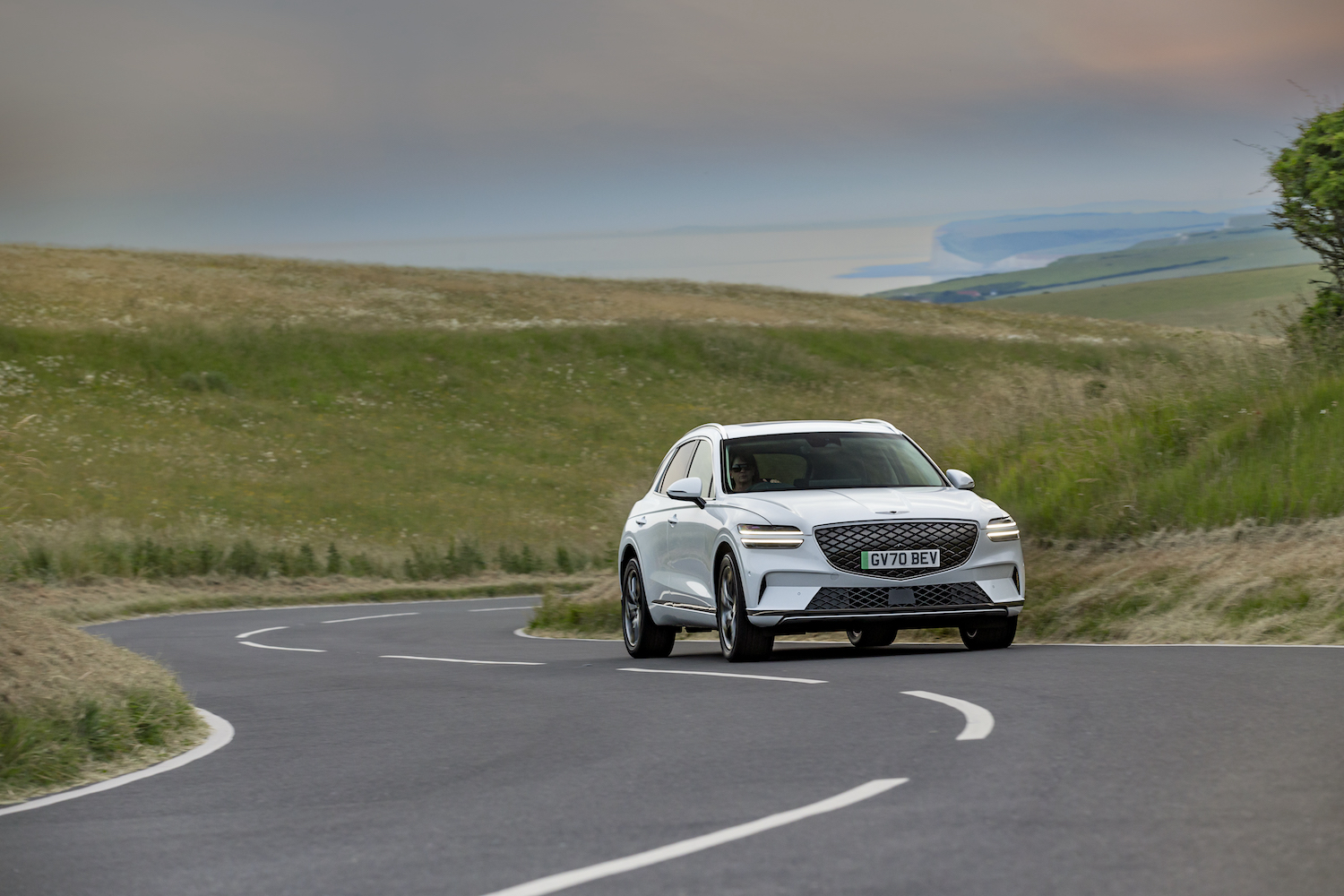 The Genesis GV70 Electrified driving on an open road with green hills in the rear