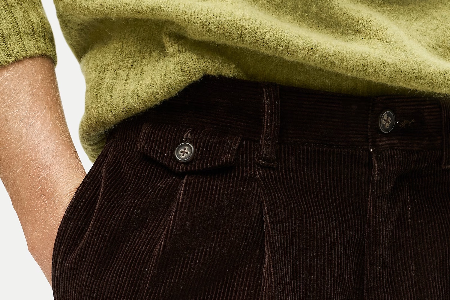 Close-up of a person's arm in a fuzzy green sweater, hand in the pocket of pleated brown corduroy pants.