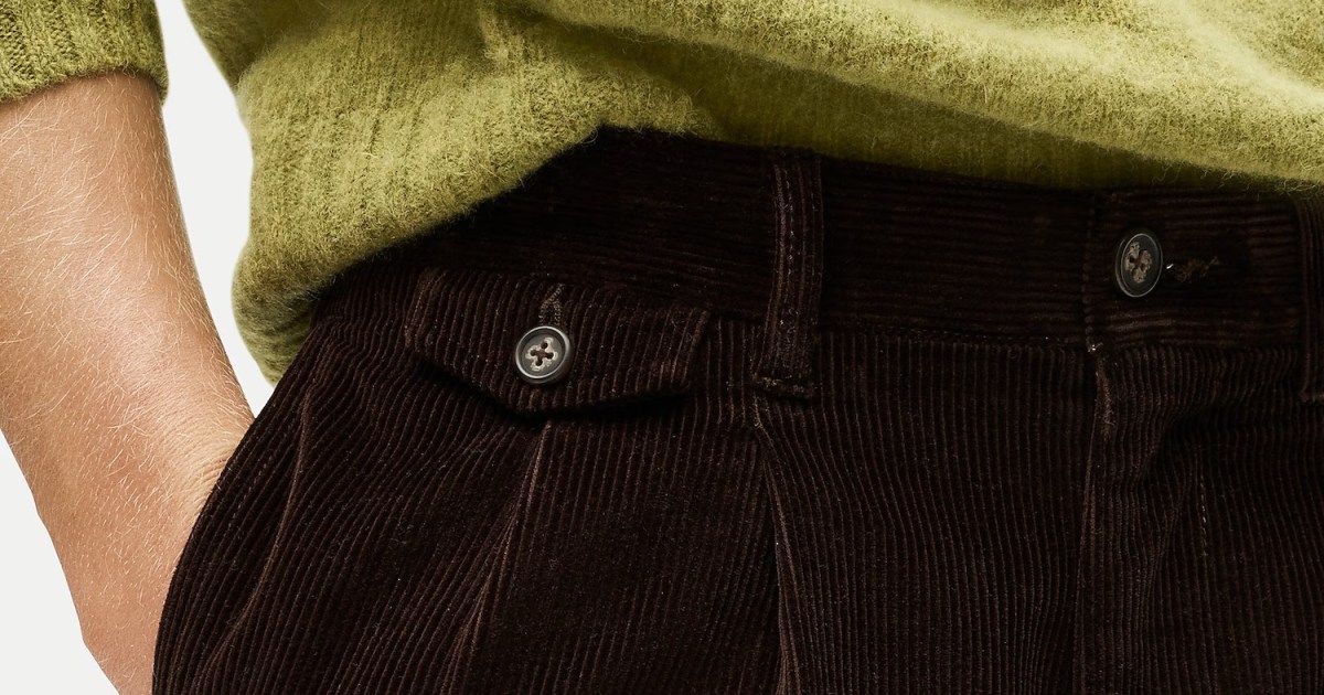 Close-up of a person's arm in a fuzzy green sweater, hand in the pocket of pleated brown corduroy pants.