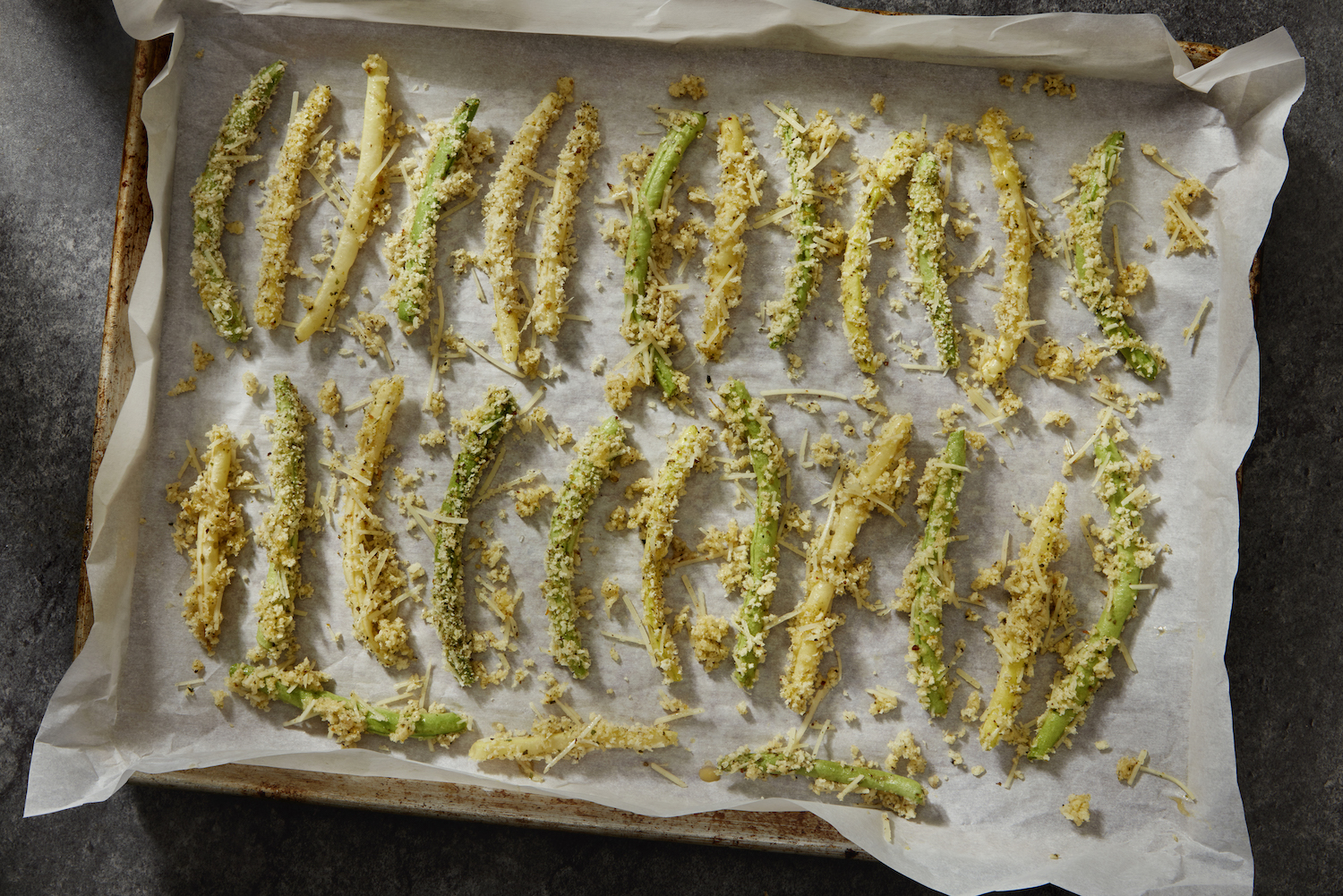 Crispy Parmesan, Panko, Garlic Crusted Yellow and Green Been Fries on a parchment-lined baking sheet