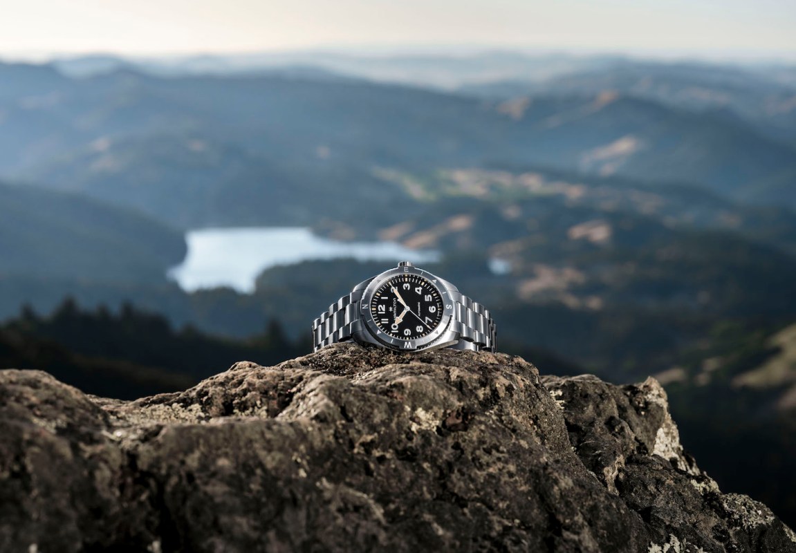 Silver watch on a cliff in front of water landscape
