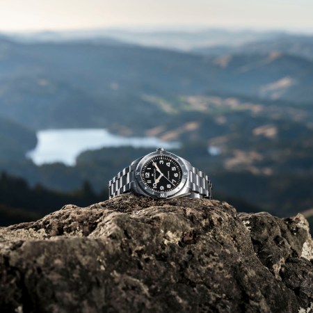 Silver watch on a cliff in front of water landscape