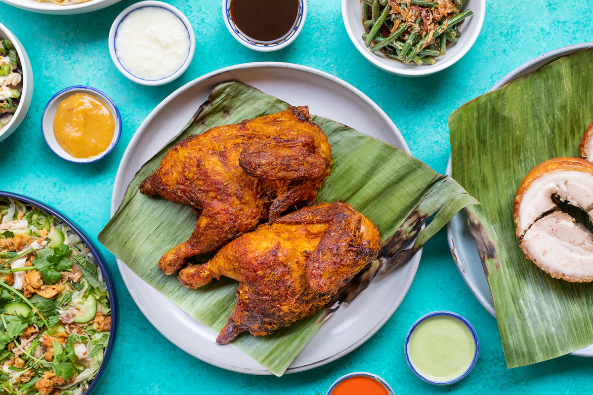 Chicken inasal on a blue table surrounded by side dishes at Lasita in Los Angeles