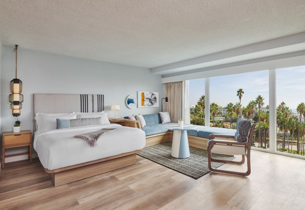 Hotel room with a bed, furniture and floor-to-ceiling windows with a view of palm trees and beach