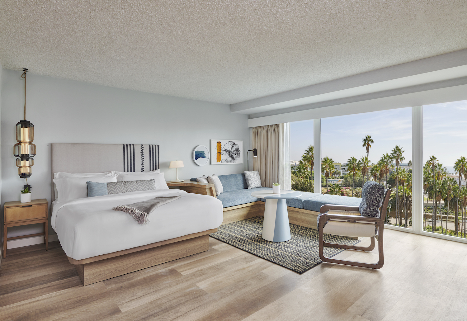 Hotel room with a bed, furniture and floor-to-ceiling windows with a view of palm trees and beach
