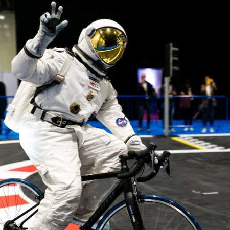 A man in spacesuit riding on a bike that has METL wheels, utilizing material that was developed by NASA