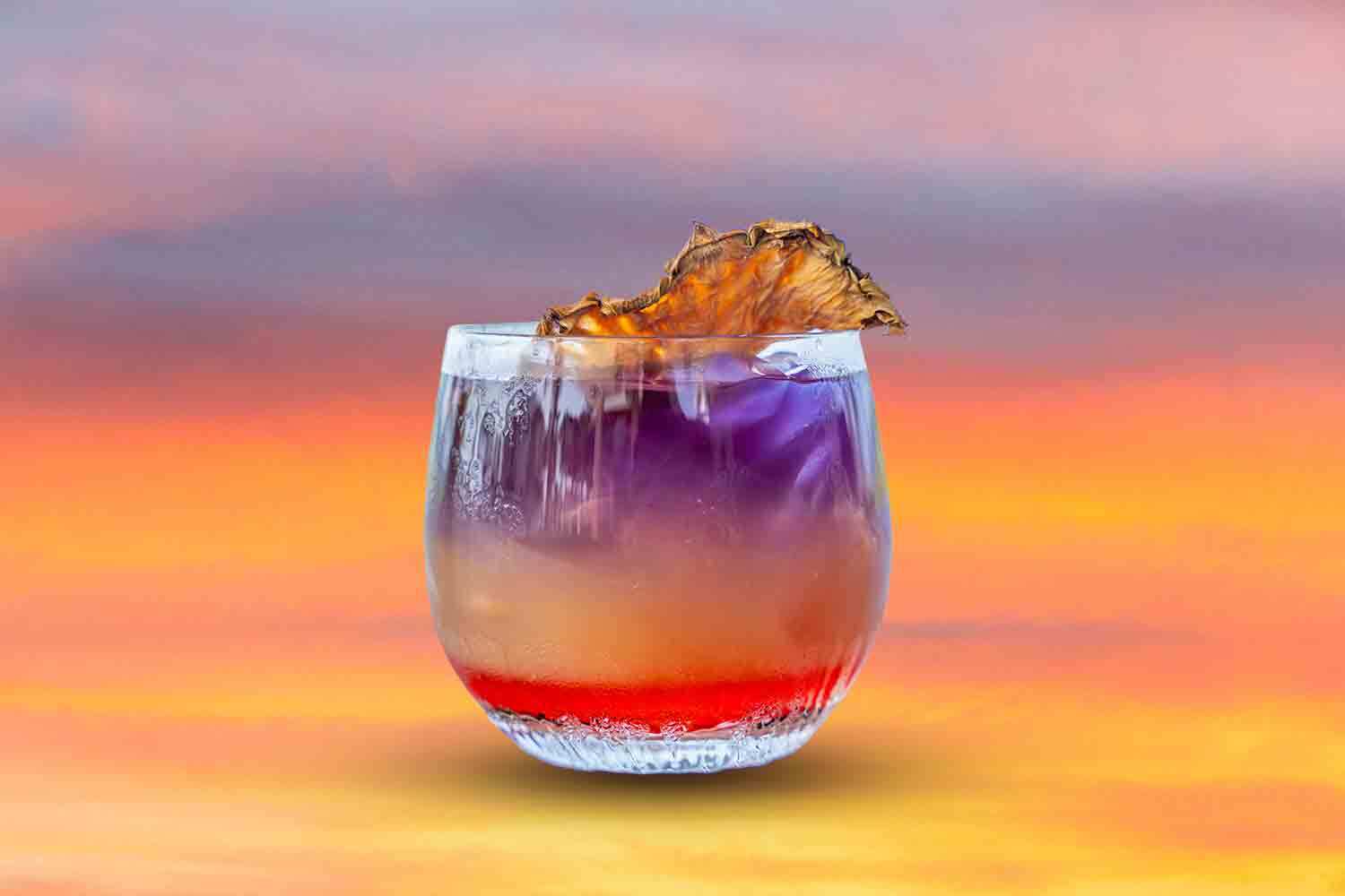 a layered cocktail in front of a sunset gradient