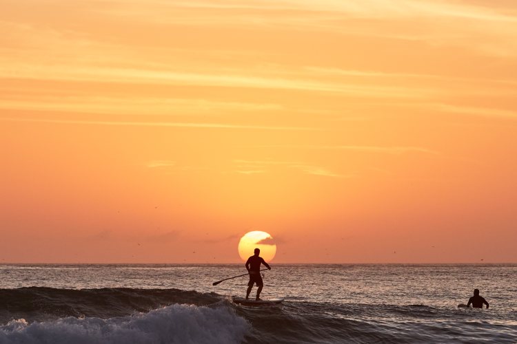 A man on a SUP board against a setting sun.