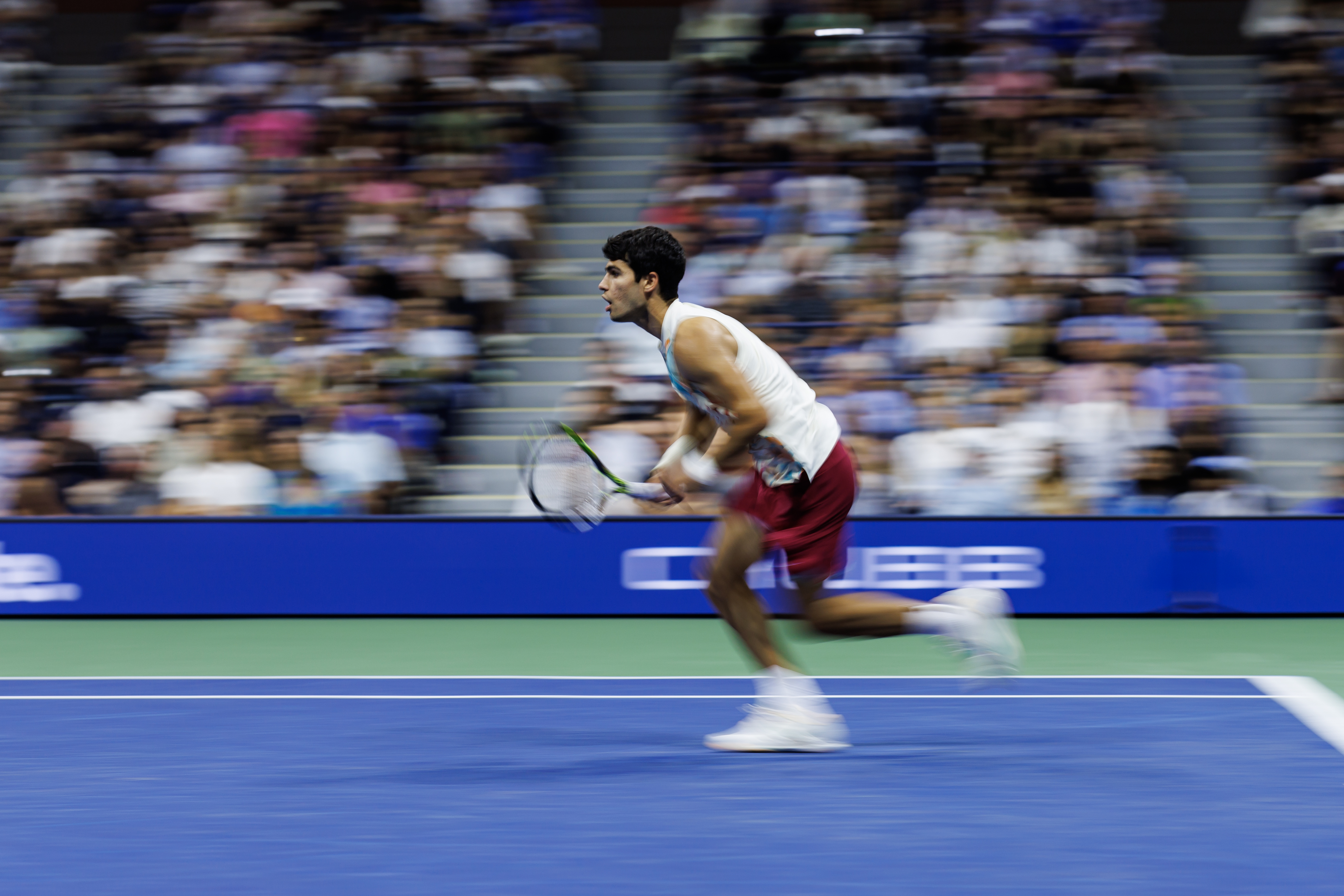A photo of Carlos Alcaraz running for the tennis ball, with his mouth open.