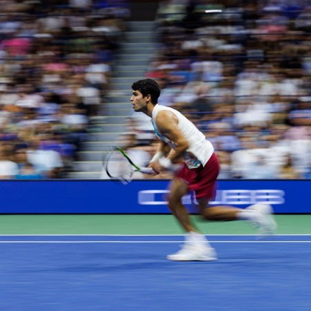 A photo of Carlos Alcaraz running for the tennis ball, with his mouth open.