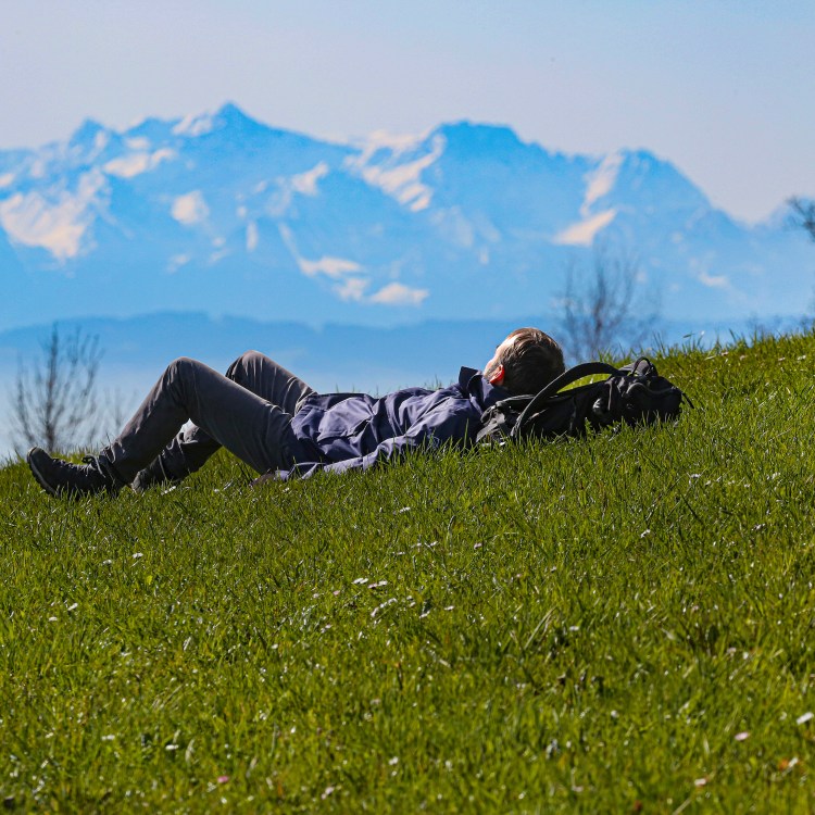A man laying in the grass with mountains in the distance. The 20-5-3 Rule suggests spending more time in nature.
