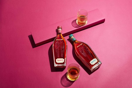 The new 2023 Cask Strength releases from Angel's Envy, with two glasses, lying on a pink tabletop