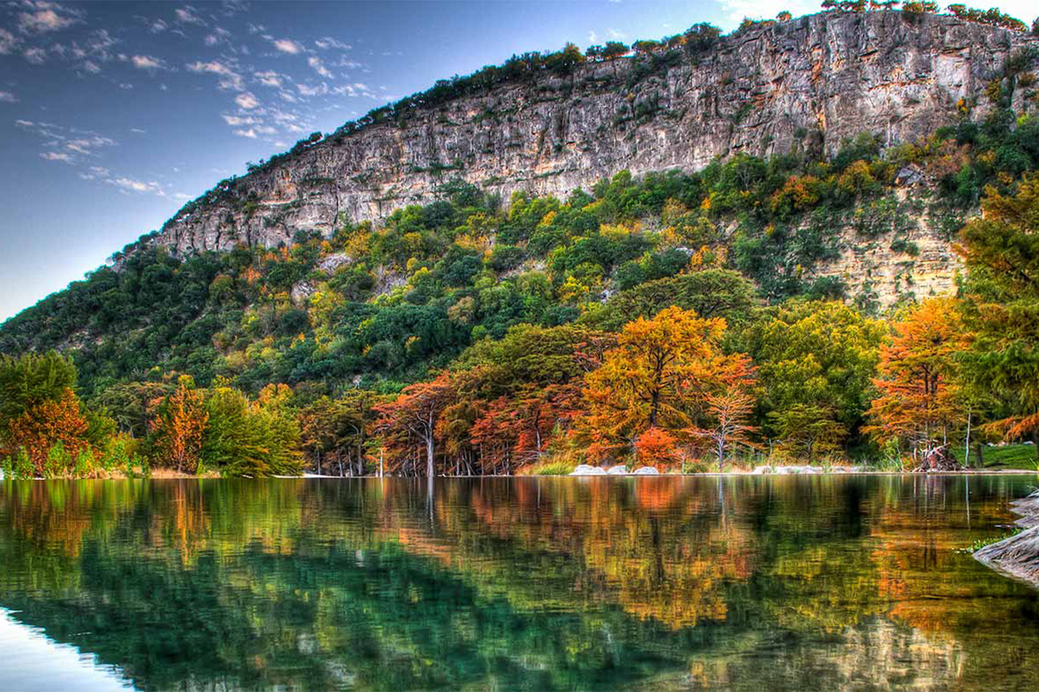 Trees changing covers in front of a mountain and reflecting in pond in front of them